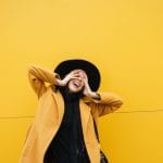 A young and stylish woman against a yellow background, shy about asking getting STD tested while on her period.