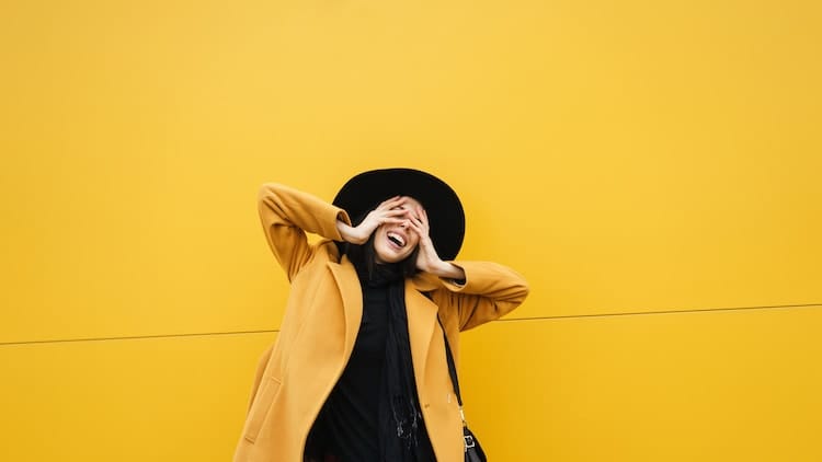 A young and stylish woman against a yellow background, shy about asking getting STD tested while on her period.