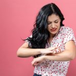 A young woman scratching her arm, similar to someone with scabies.