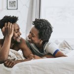 Black couple in bed, looking at one another with love.