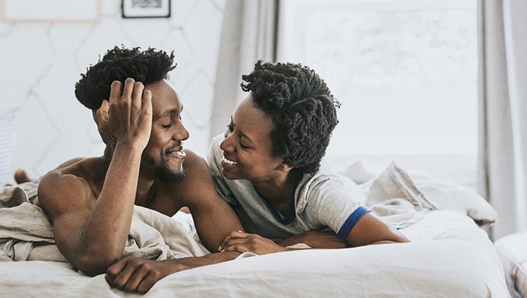 Black couple in bed, looking at one another with love.