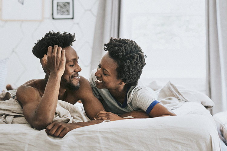 Black couple in bed, looking at one another with love.