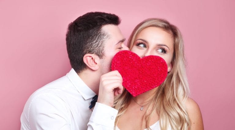 Young couple holding red love heart over eyes and kissing
