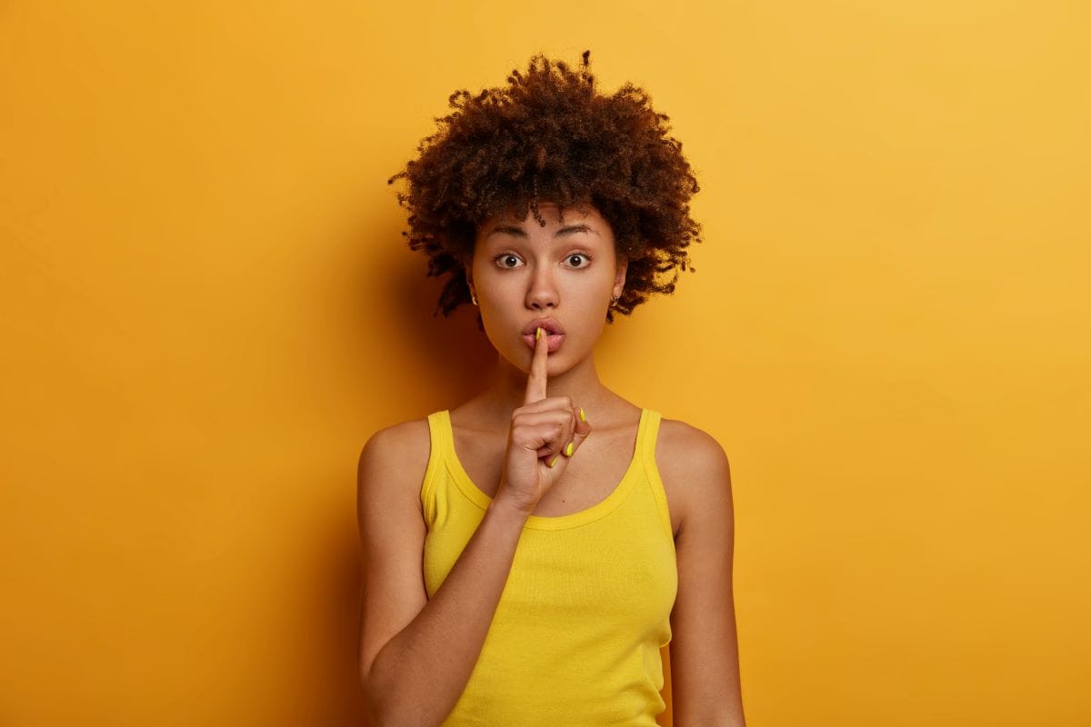 African American woman presses index finger to lips, asks be quiet